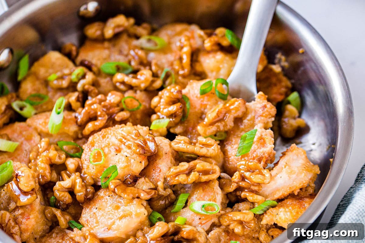 A close-up view of Honey Walnut Shrimp still in the skillet, with a serving scoop lifting a portion of the dish.