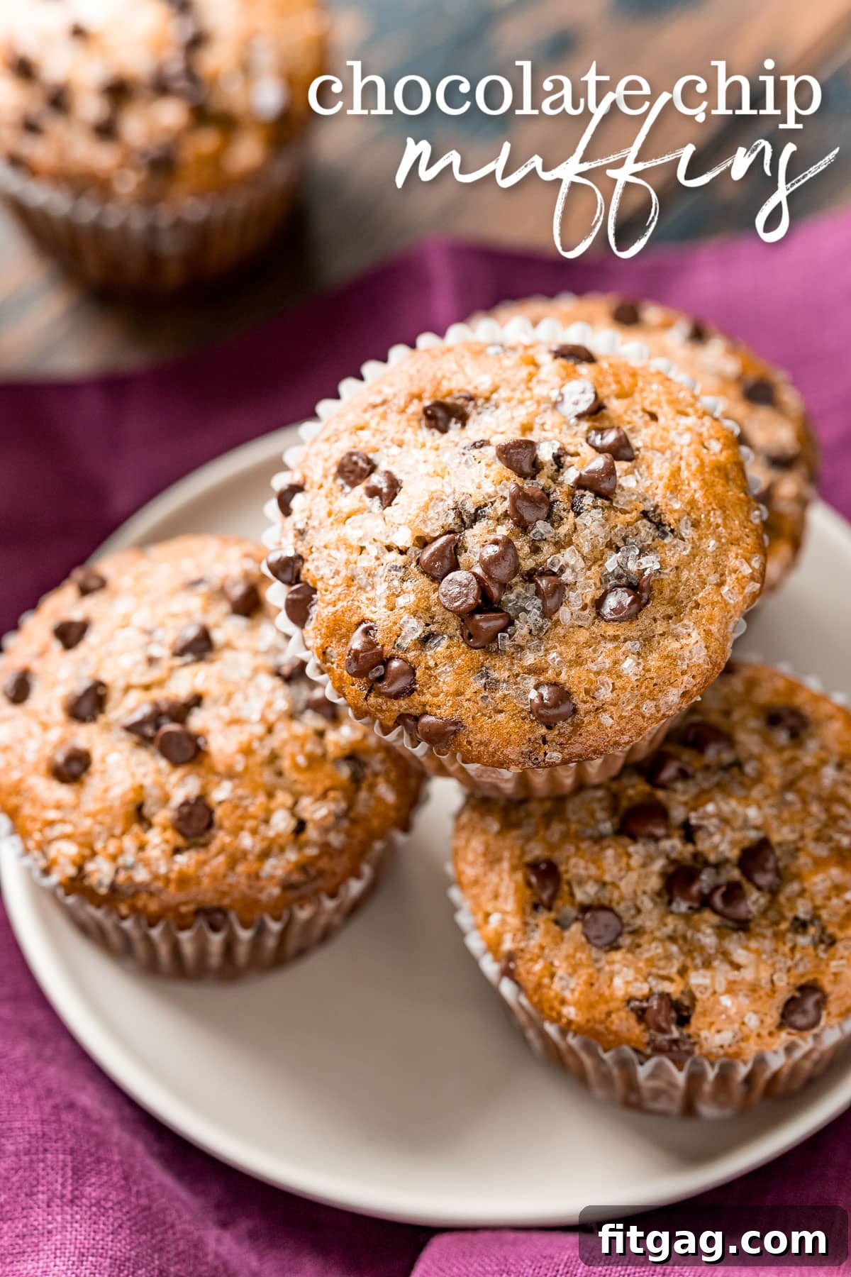 Effortless Chocolate Chip Muffins 2 Four golden-brown chocolate chip muffins arranged on a white plate, with a rich burgundy napkin elegantly placed beneath. A title overlay at the top reads 'Chocolate Chip Muffins'.