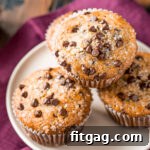 Effortless Chocolate Chip Muffins 11 Four chocolate chip muffins on a white plate with a burgundy napkin beneath the plate