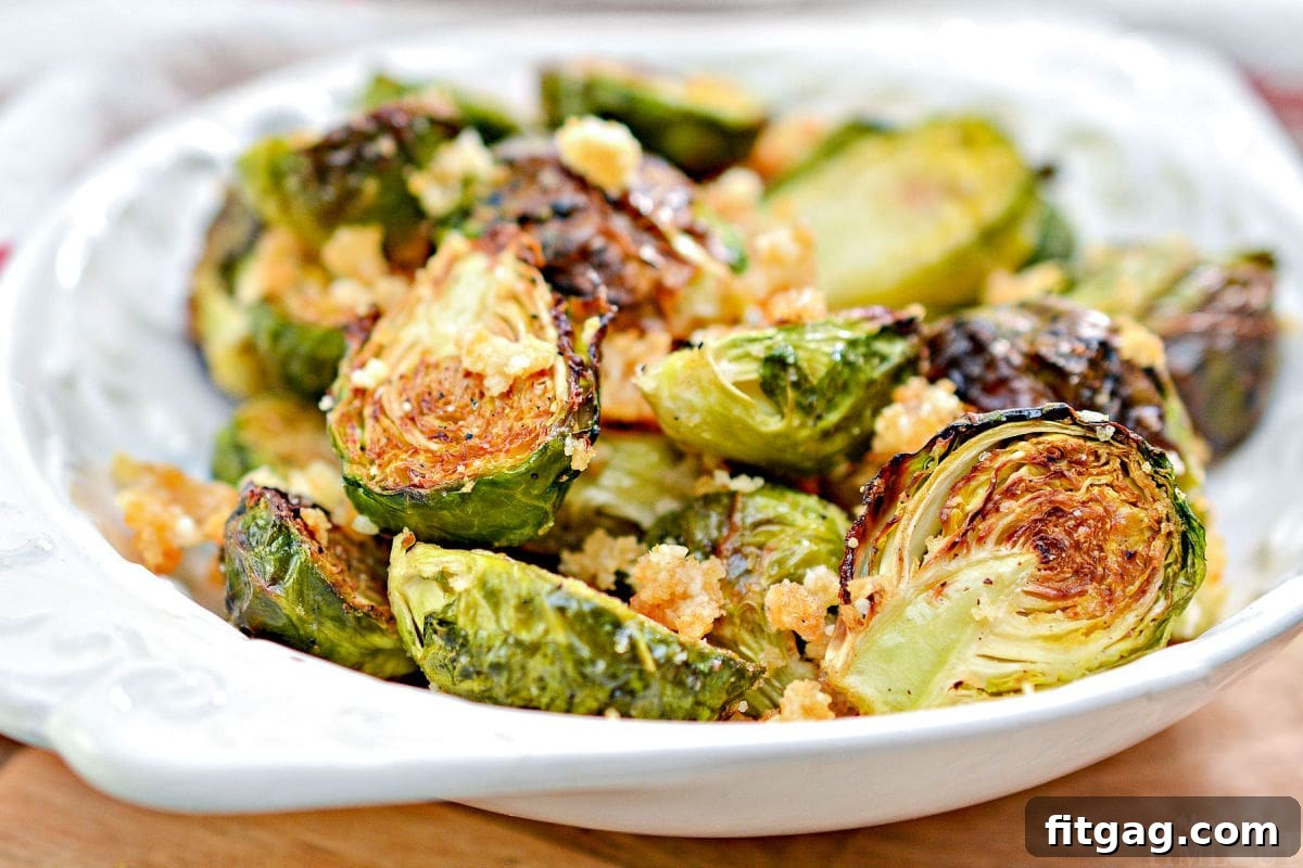Close-up of golden brown air fried Brussels sprouts with grated Parmesan and garlic in a shallow white bowl.