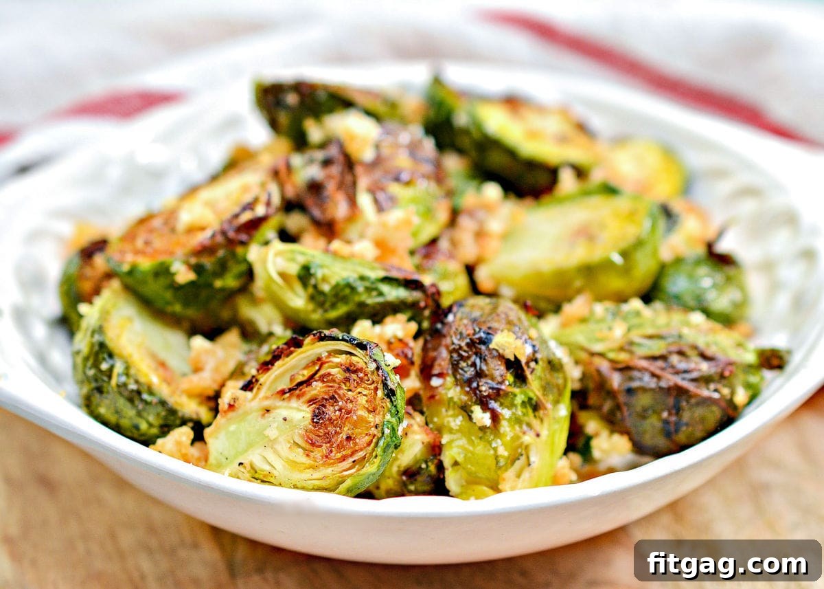 Crispy garlic parmesan air fryer Brussels sprouts in a white shallow bowl, with a red and white kitchen towel in the background.