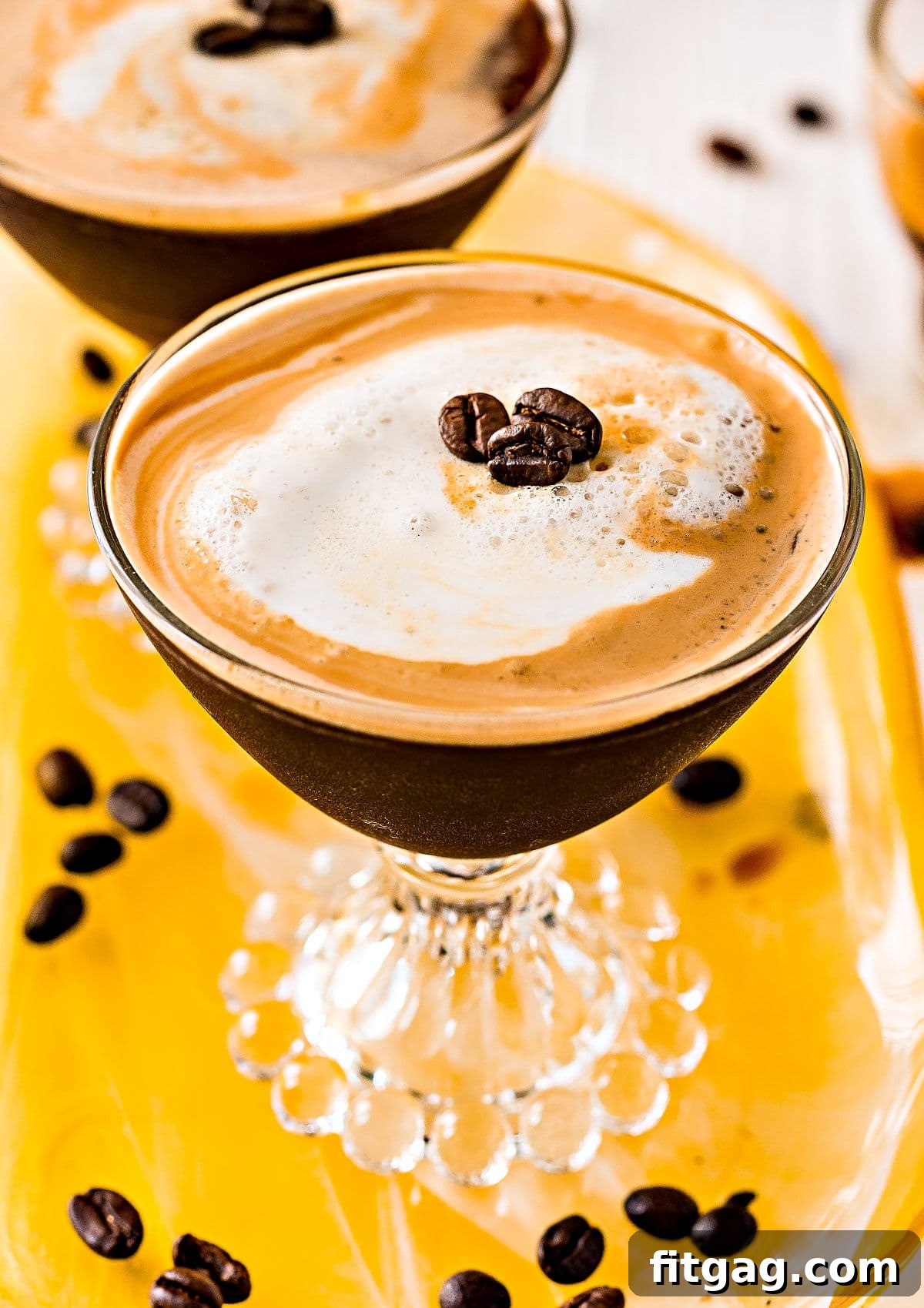 espresso martini recipe in two glasses on yellow glass tray top down view
