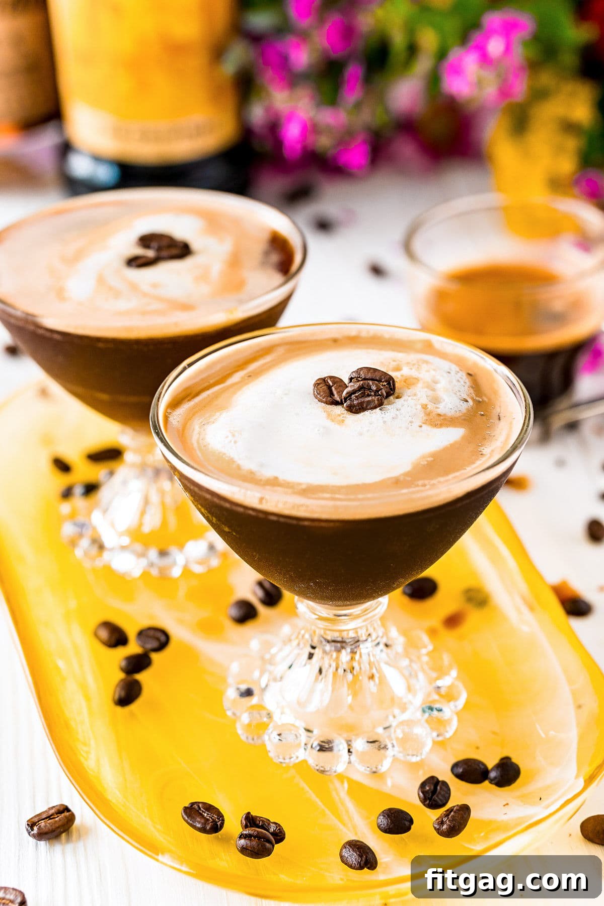two espresso martinis on a yellow glass tray with espresso beans scattered about