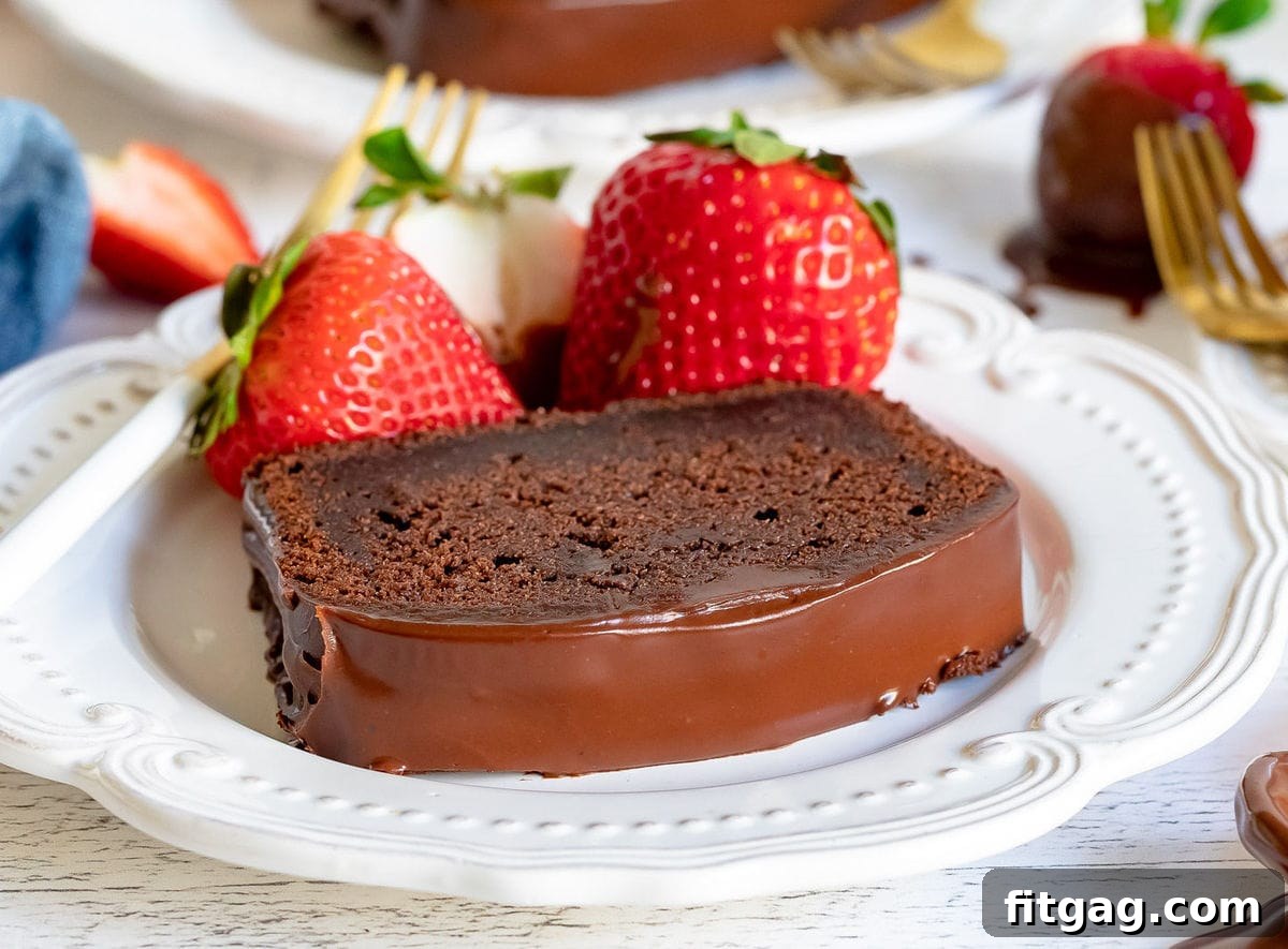 A single, inviting slice of chocolate pound cake, richly glazed and garnished with fresh strawberries, served on a white plate, highlighting its moist interior and perfect presentation.