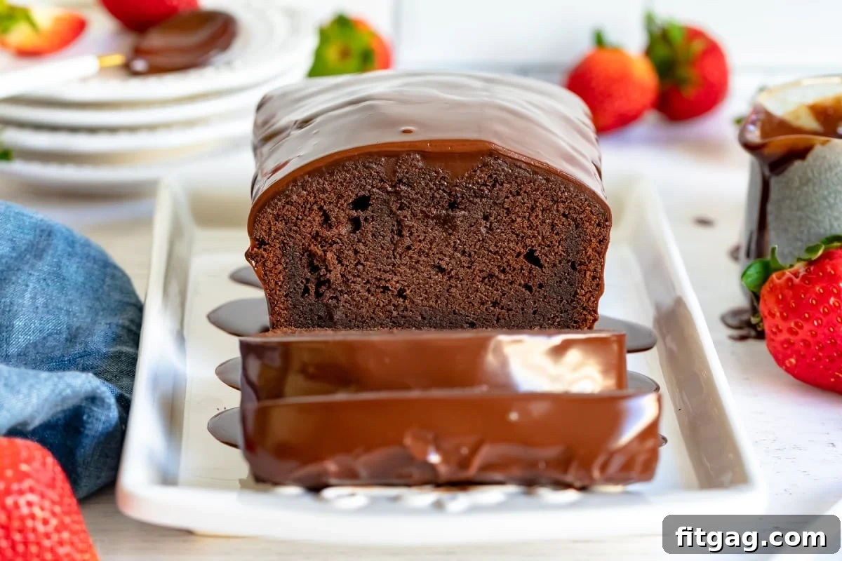 A perfectly baked chocolate pound cake, with three slices already cut, presented on a pristine white platter alongside golden forks and fresh strawberries, all set against a soft blue napkin for a touch of elegance.