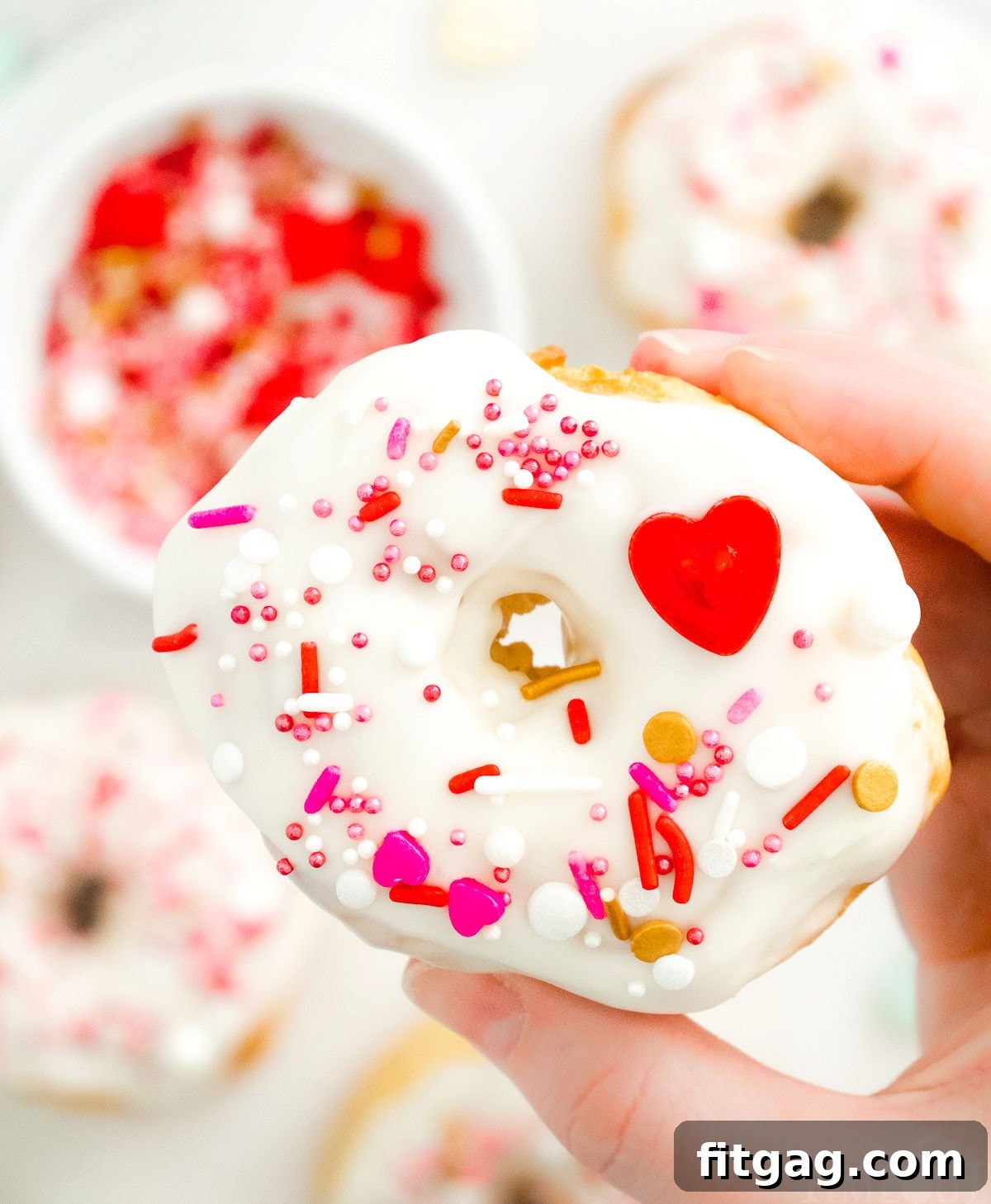 A beautifully decorated air fryer donut being held over a tray of freshly glazed donuts.