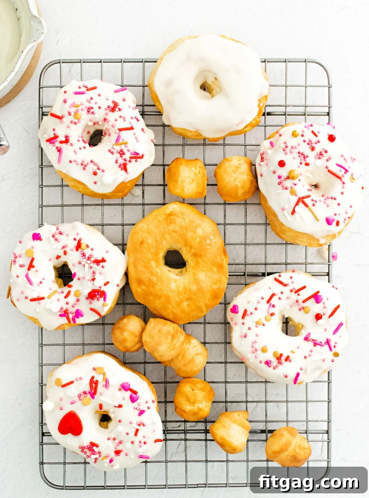 Freshly air-fried donuts cooling on a wire rack, some already glazed and adorned with sprinkles.