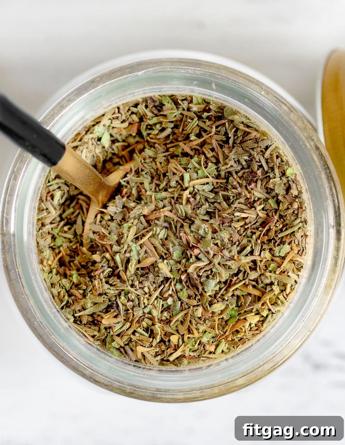 A top-down view of a glass jar filled with mixed Italian seasoning herbs.