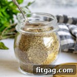 Italian seasoning in a small glass jar with a spoon.