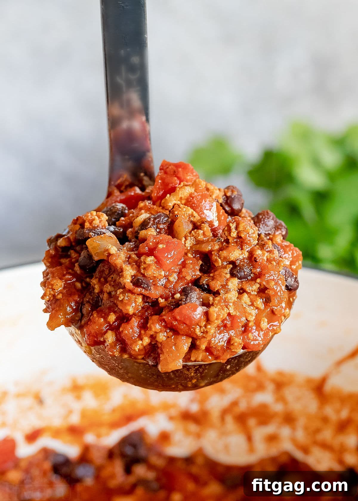 ladle of chili being held up above the pot.