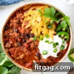 bowl of turkey chili with cheddar cheese sour cream cilantro and green onions.