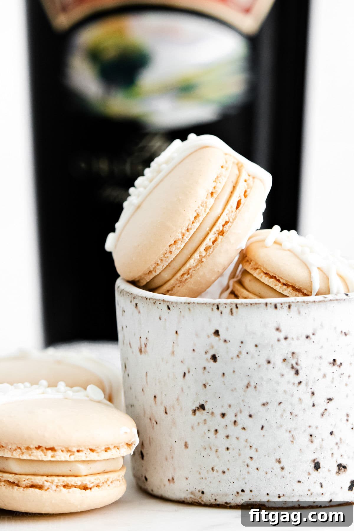 macarons with a creamy Irish cream filling in small white bowl with bottle of Bailey's Irish cream in background.