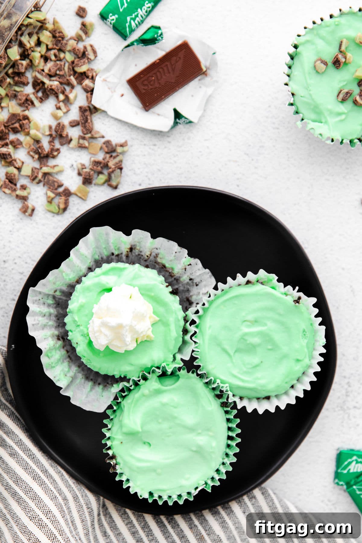 top down look at green mini cheesecakes on a black plate one topped with whipped cream.