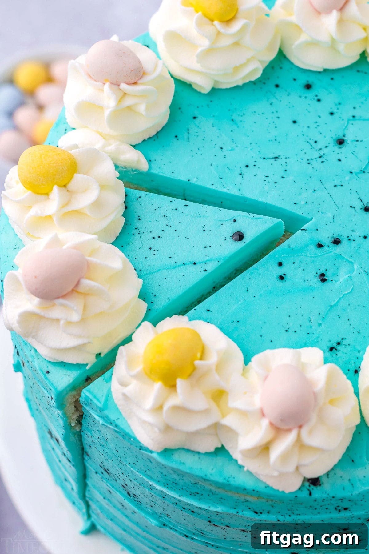 A top-down view of the Speckled Egg Easter Cake, beautifully frosted in blue with one slice carefully cut out, revealing the soft vanilla interior.