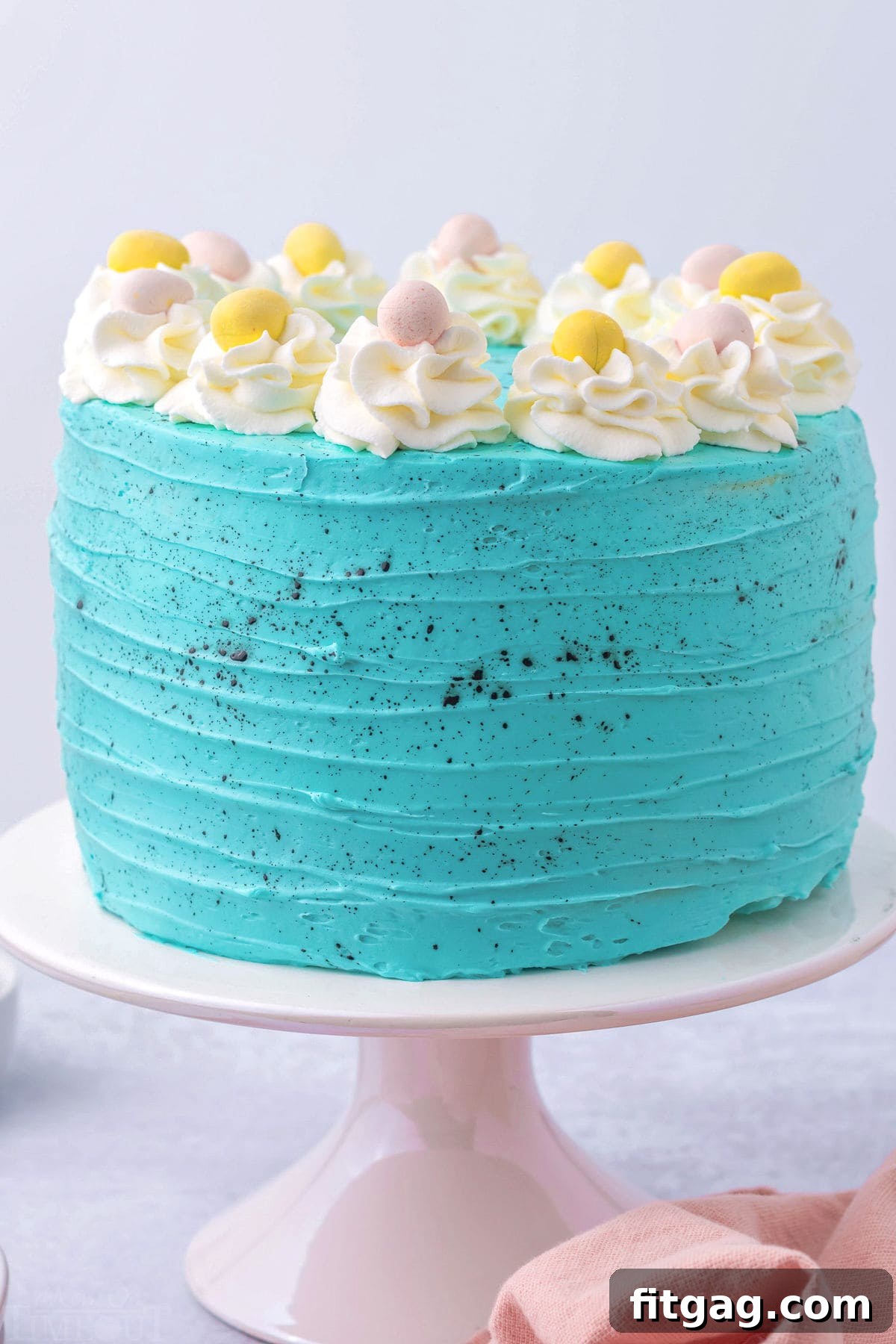 A whole, perfectly decorated Speckled Egg Easter Cake, featuring smooth turquoise frosting and a scattering of mini Cadbury eggs on top, ready for serving.