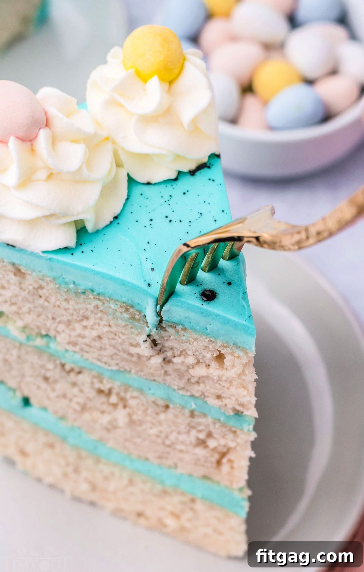 A fork gently piercing a slice of the Speckled Egg Easter Cake, showing the soft, moist interior and the vibrant blue frosting.