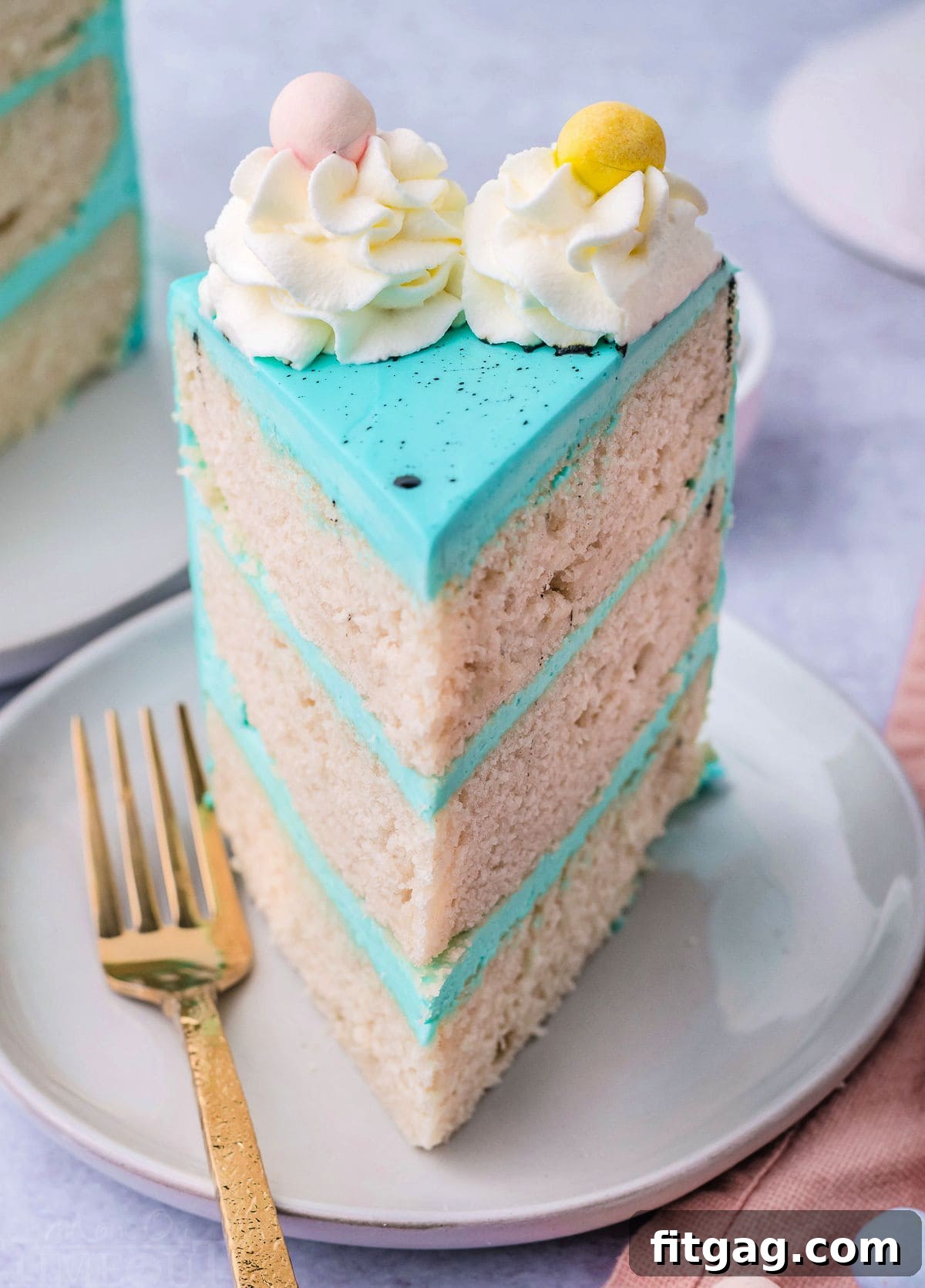 A single slice of the beautiful vanilla Easter cake, with vibrant turquoise frosting and a scattering of mini Cadbury eggs on top.
