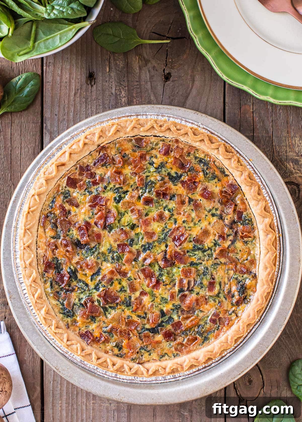 A beautiful top-down view of a whole spinach quiche, golden brown and ready to slice, resting on a rustic wooden surface.