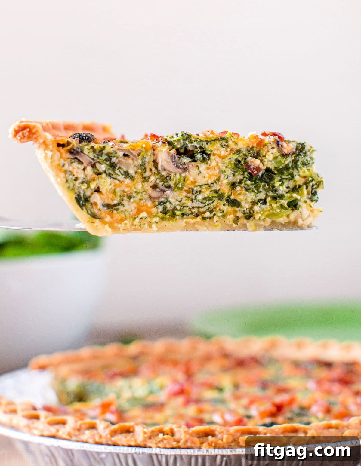 A perfect slice of spinach mushroom quiche carefully lifted from the pie plate, showing its rich filling and golden crust.