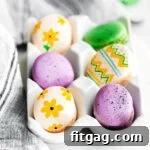 French macarons decorated as Easter eggs sitting in a white egg crate.
