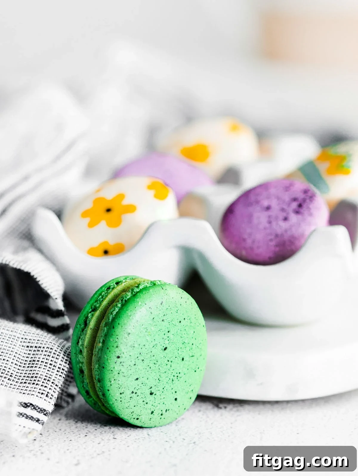 Green speckled macaron sitting in front of an egg tray.