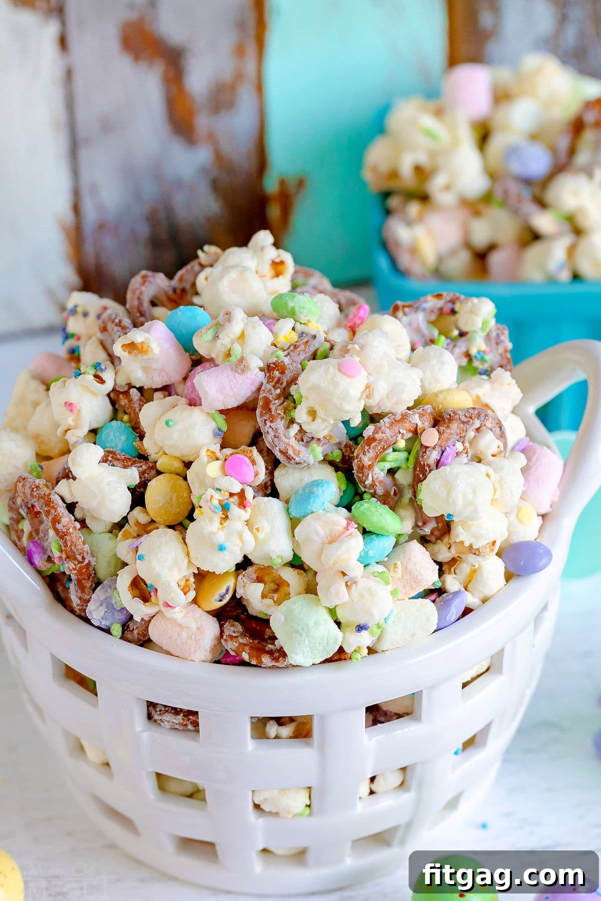 Hoppy Easter Snack Blend 7 A festive white ceramic basket filled with Bunny Bait Easter Snack Mix, featuring popcorn, pretzels, M&Ms, and colorful marshmallows.