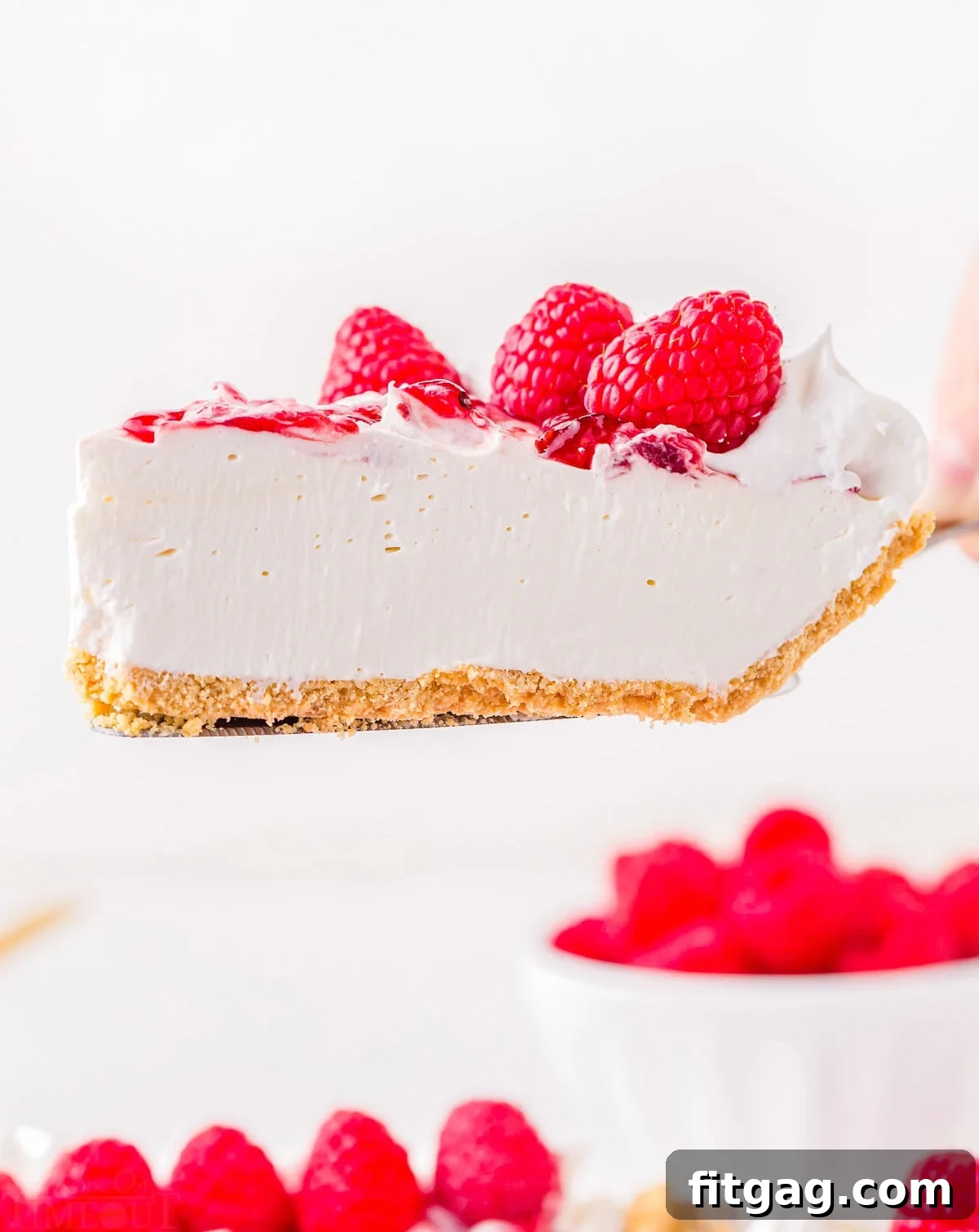 A slice of raspberry no-bake cheesecake being held up by a pie server, showcasing its creamy texture and vibrant swirl.