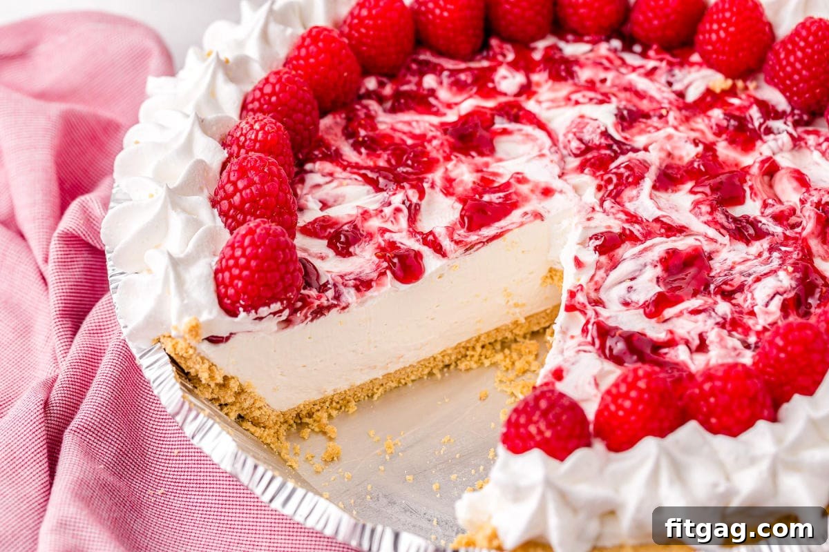A whole raspberry cheesecake with one slice removed, resting next to a pink kitchen towel.