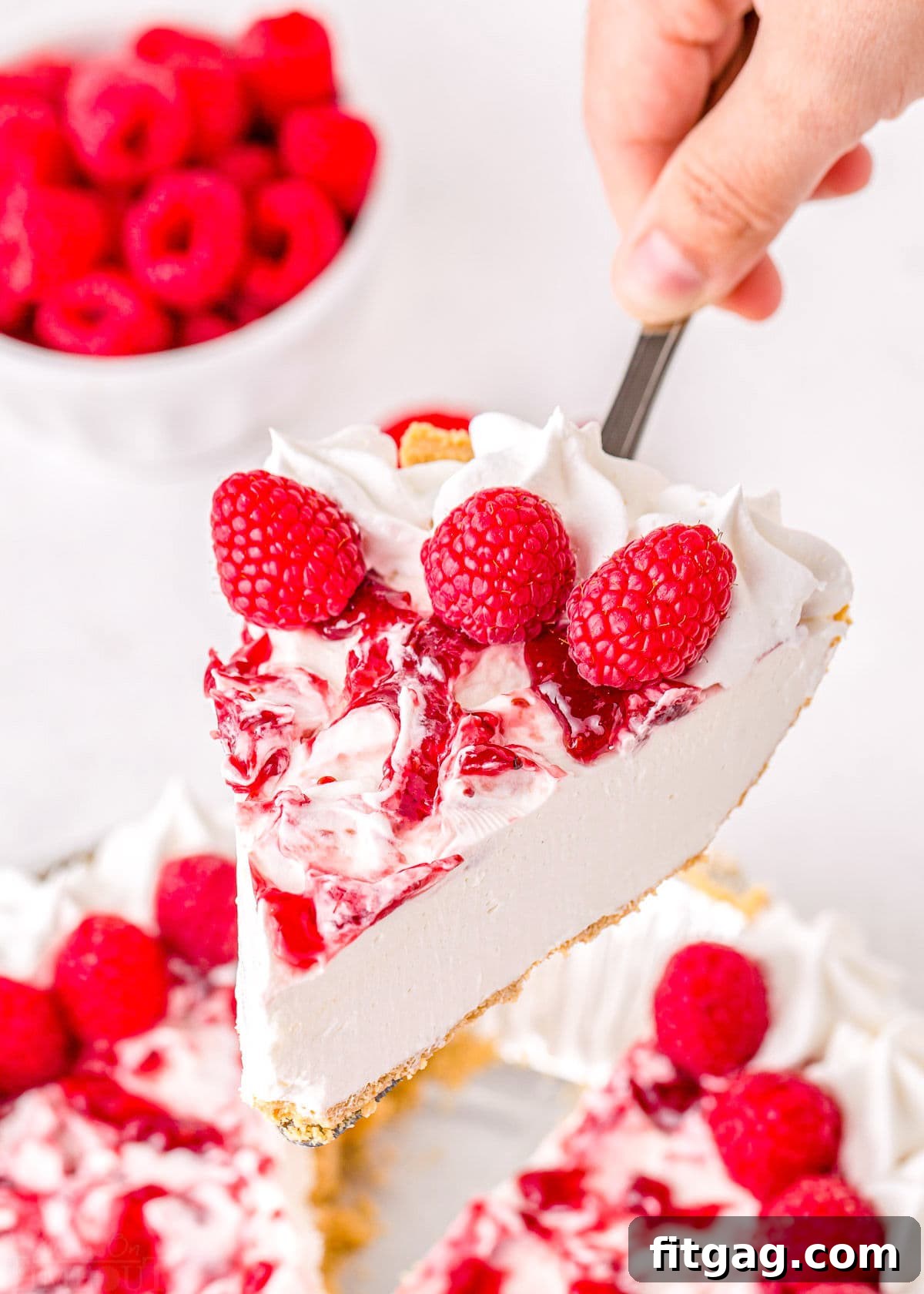 A slice of no-bake raspberry cheesecake with raspberry topping being served with a pie server over the rest of the cake.