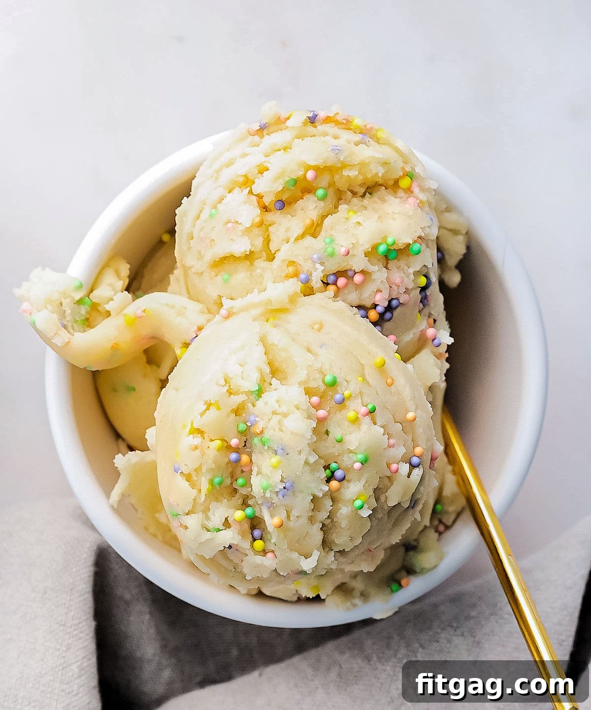 No-Bake Sugar Cookie Bliss 3 top down look at cookie dough with sprinkles in small white bowl with gold spoon.