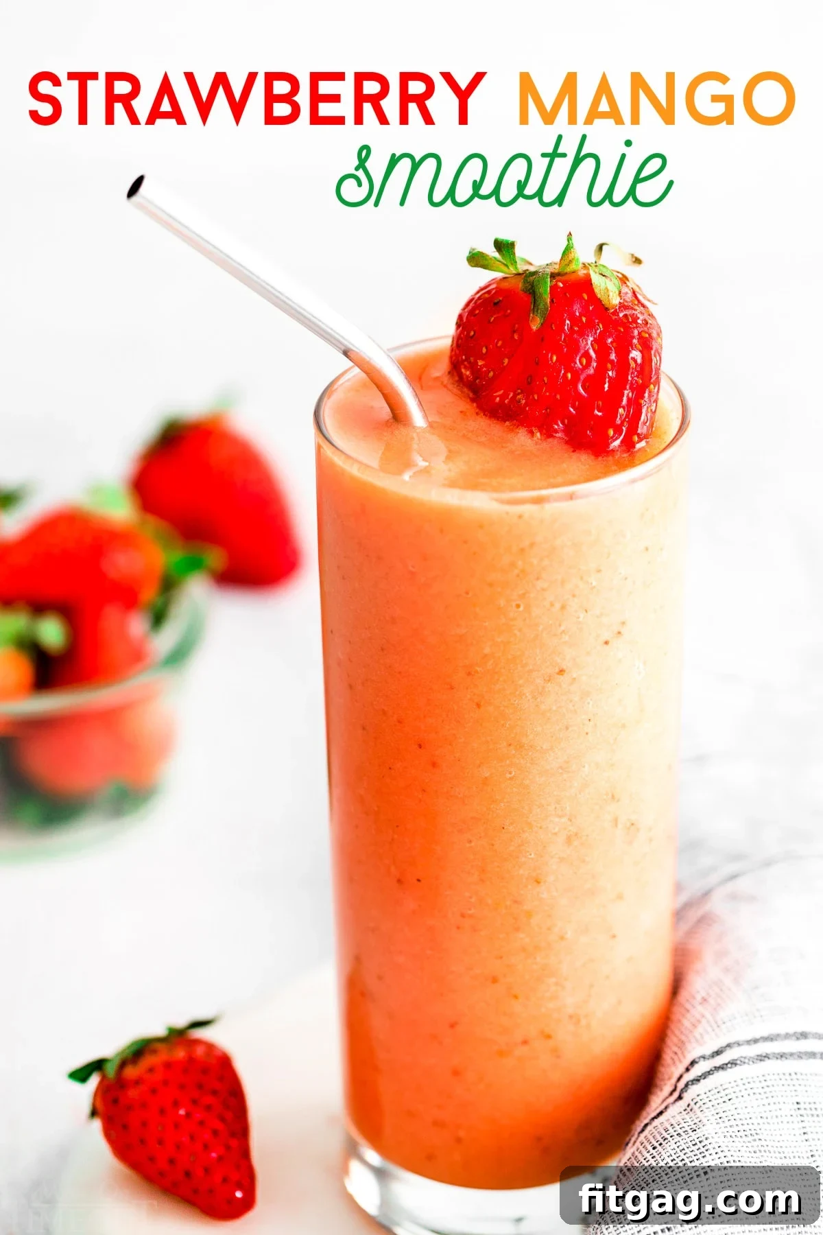 A vibrant strawberry mango smoothie in a tall glass with a steel straw, garnished with fresh strawberry slices, set against a bright background.