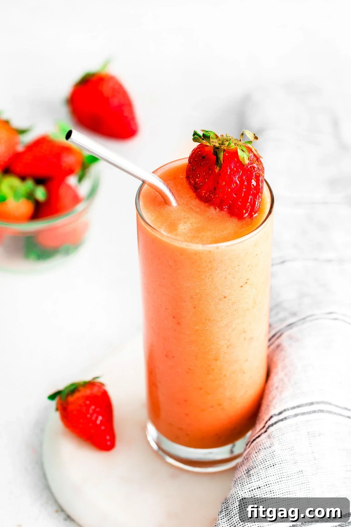 A vibrant strawberry mango smoothie in a tall glass, elegantly placed on a clean white surface, highlighting its appealing color and texture.