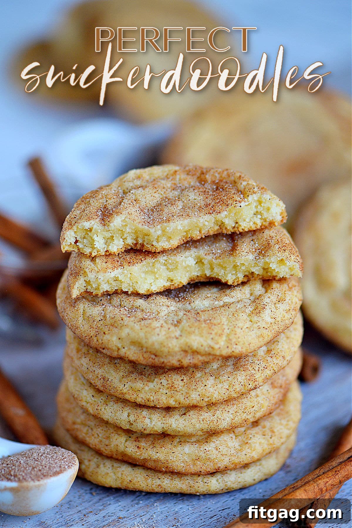 Stacked soft and chewy snickerdoodle cookies on a rustic blue board, with the top cookie broken to reveal its tender interior. A perfect visual of a delicious homemade treat.