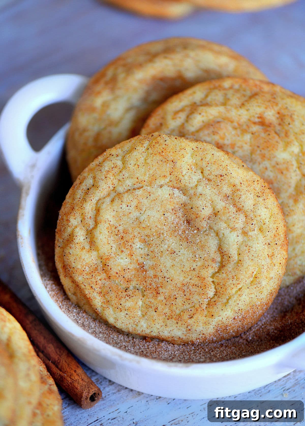 Close-up view of snickerdoodle cookie dough being thoroughly coated in a vibrant cinnamon sugar mixture in a small white bowl, preparing for baking.
