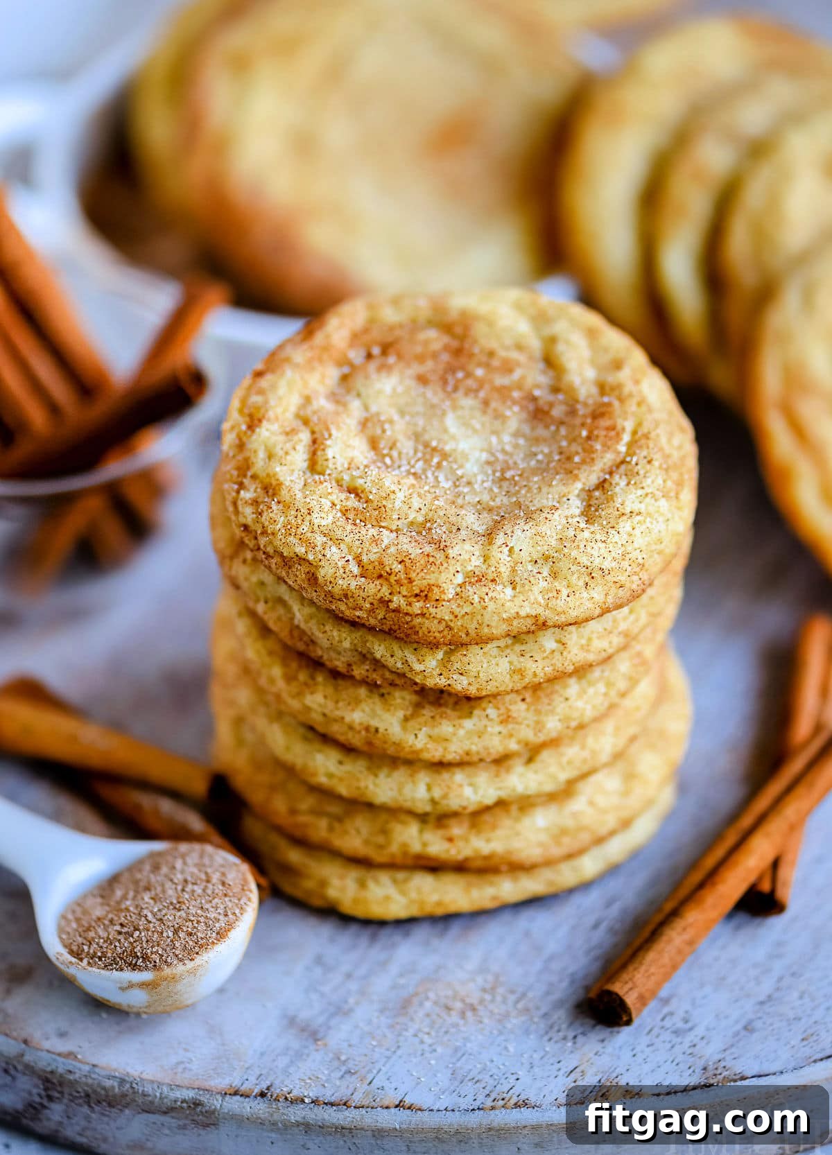 A stack of perfectly baked snickerdoodle cookies on a blue board, accompanied by fragrant cinnamon sticks, highlighting their warm, inviting appearance and classic appeal.
