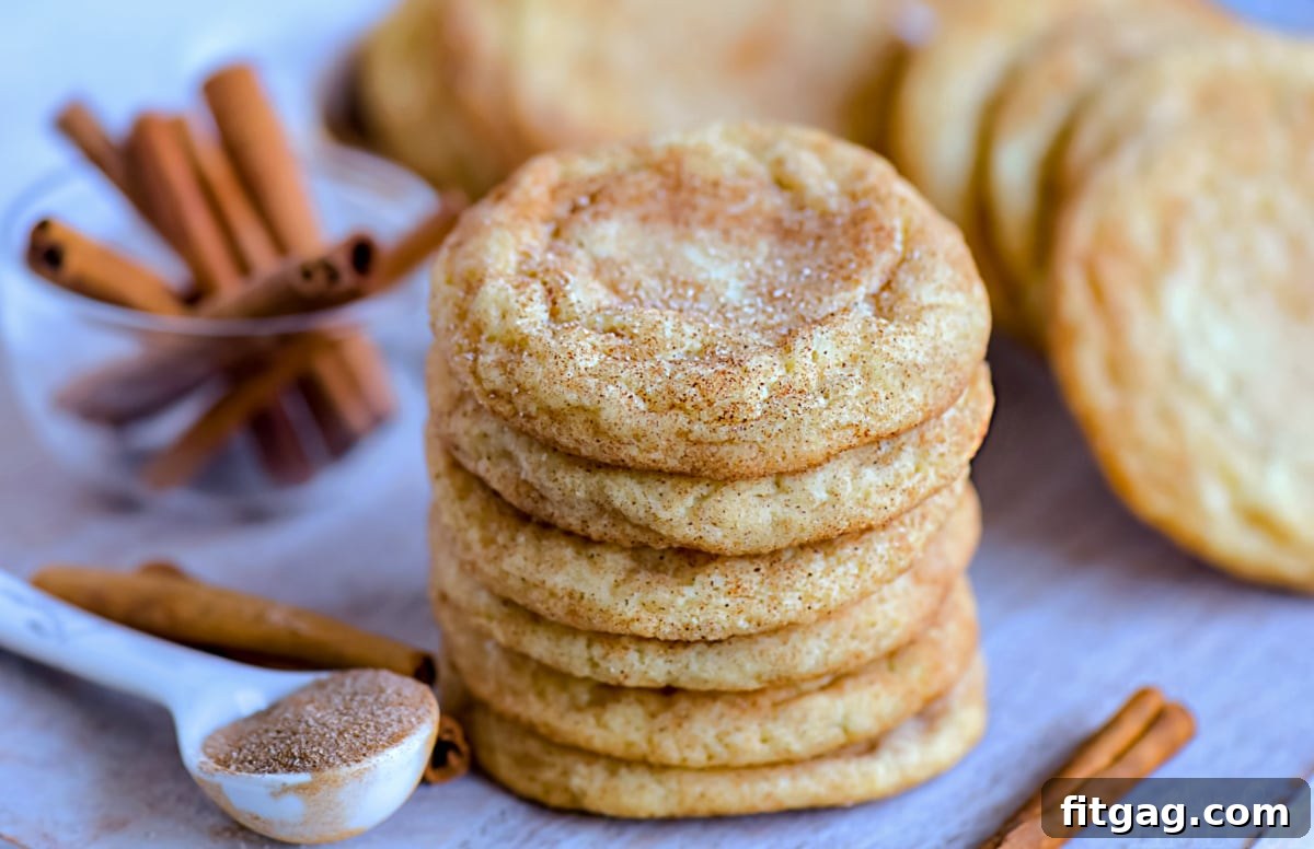 Beautifully arranged snickerdoodle cookies stacked on a wooden cutting board, with additional cookies in the background and cinnamon sticks scattered artistically, showcasing their golden-brown color and inviting, soft texture.
