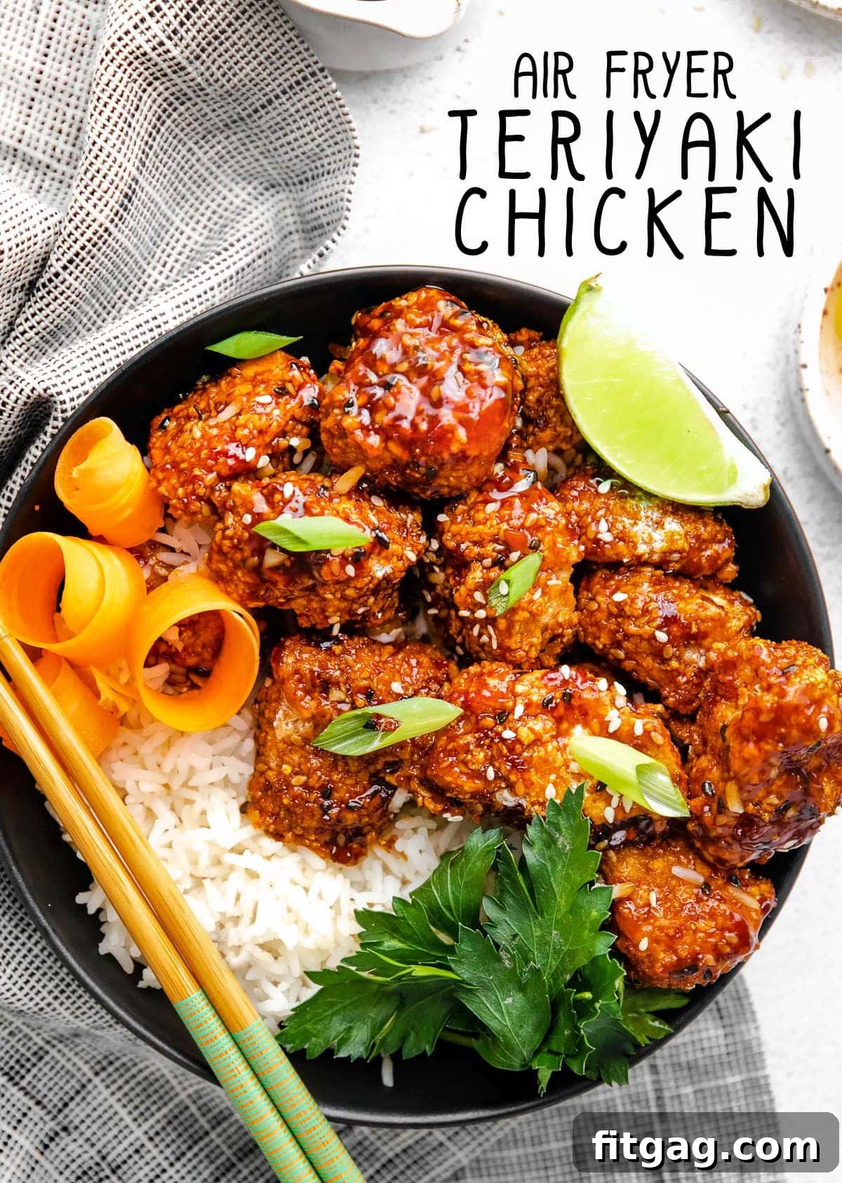 Teriyaki chicken with rice in a black bowl next to a striped black and white towel. 