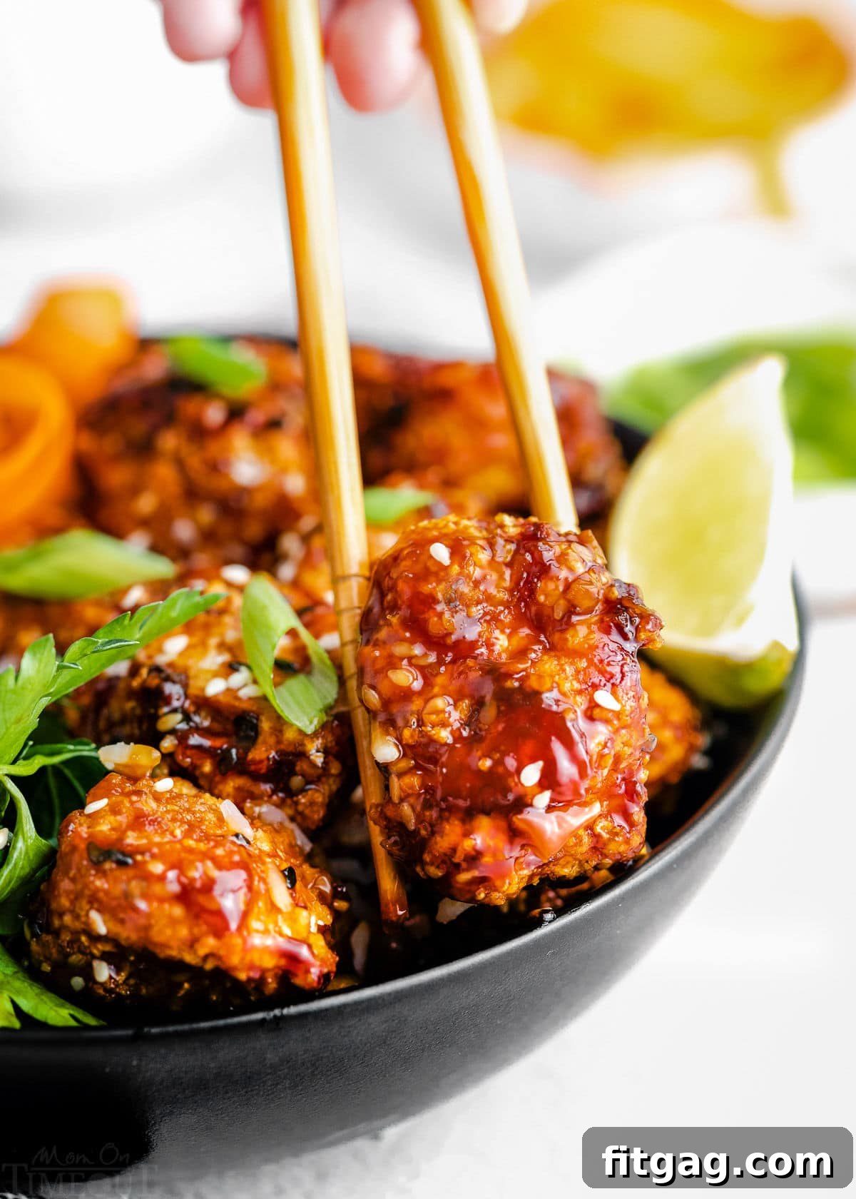 Piece of teriyaki chicken being picked up out of a bowl with chopsticks.