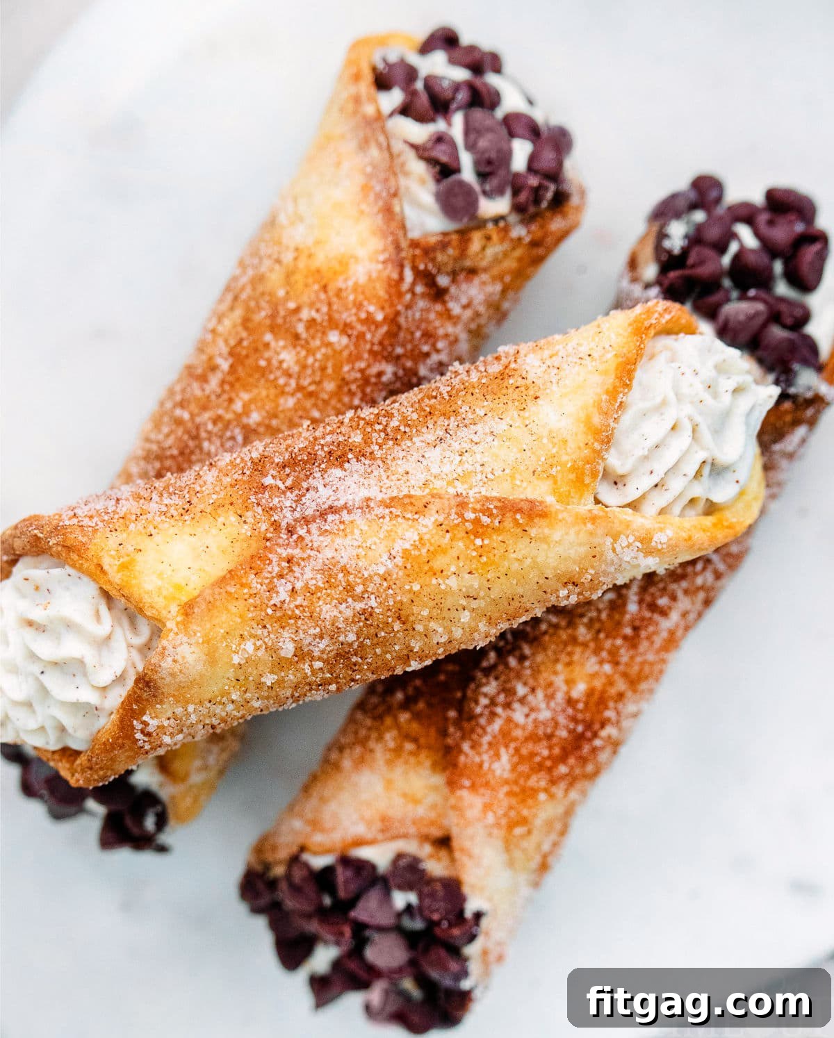 Close up look at cannolis with a churro coating. Three stacked on a white plate.