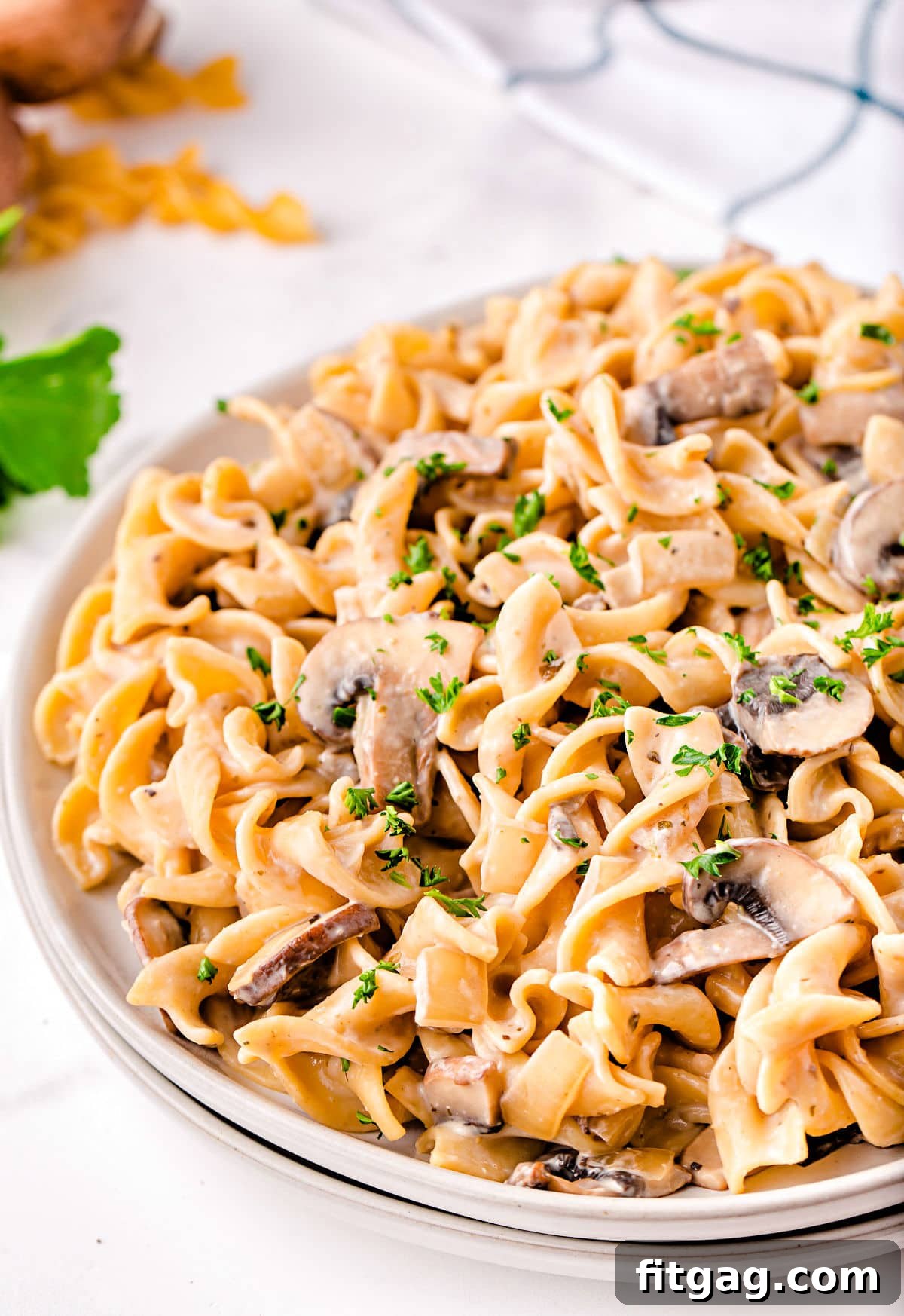 close up look at stroganoff with mushrooms on white plate with white and black towel in background.