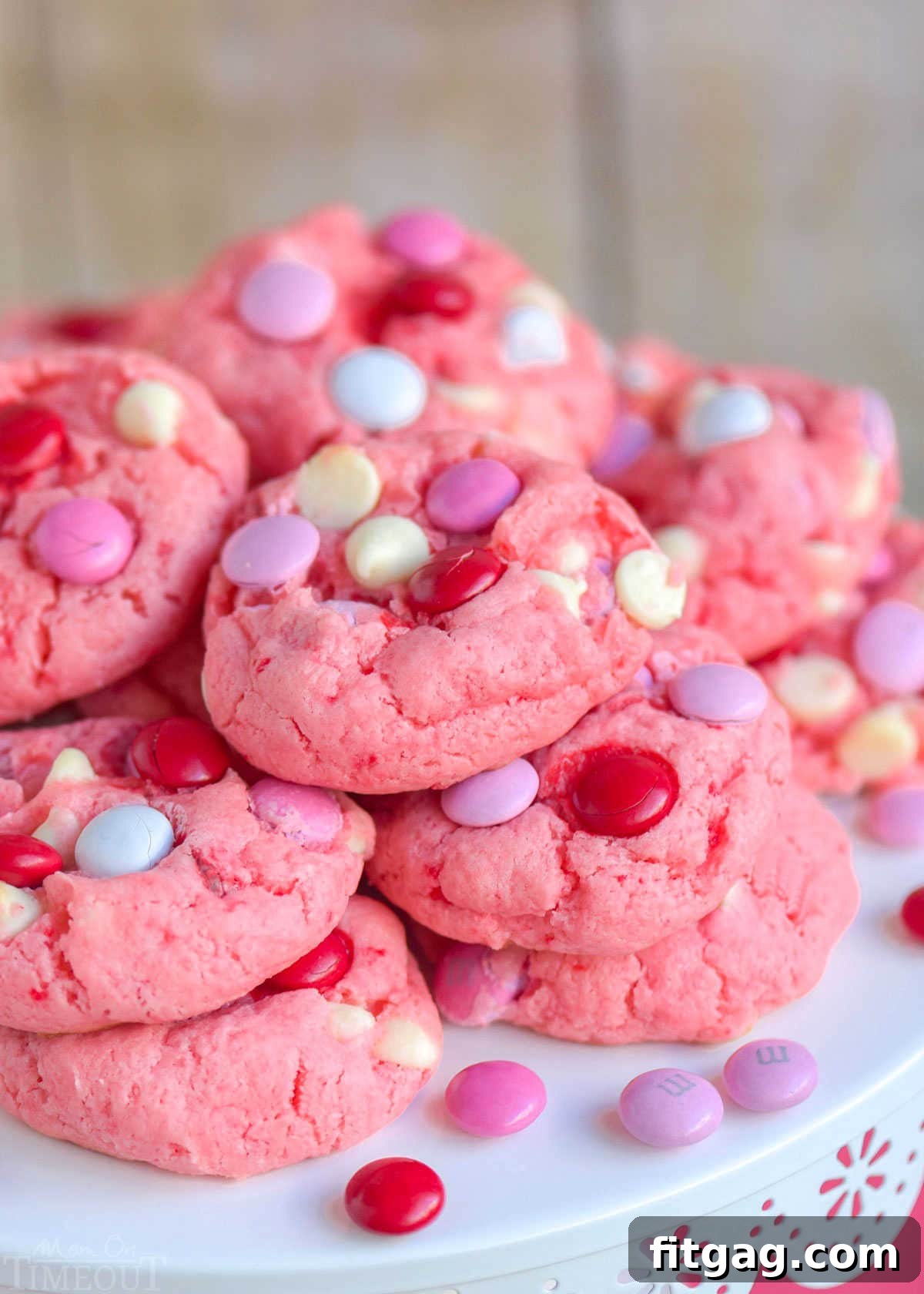 A stunning pile of super moist Strawberry Cake Mix Cookies, adorned with colorful M&Ms and creamy white chocolate chips, elegantly presented on a white metal cake stand.