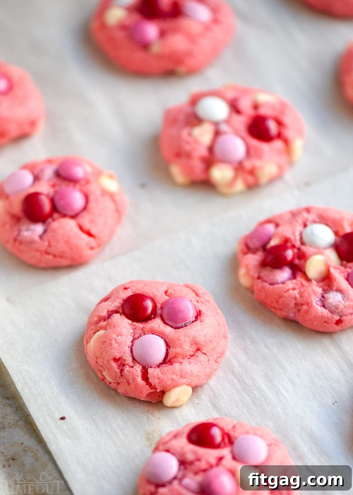 A baking sheet lined with parchment paper, holding freshly baked strawberry cake mix cookies, still warm from the oven.