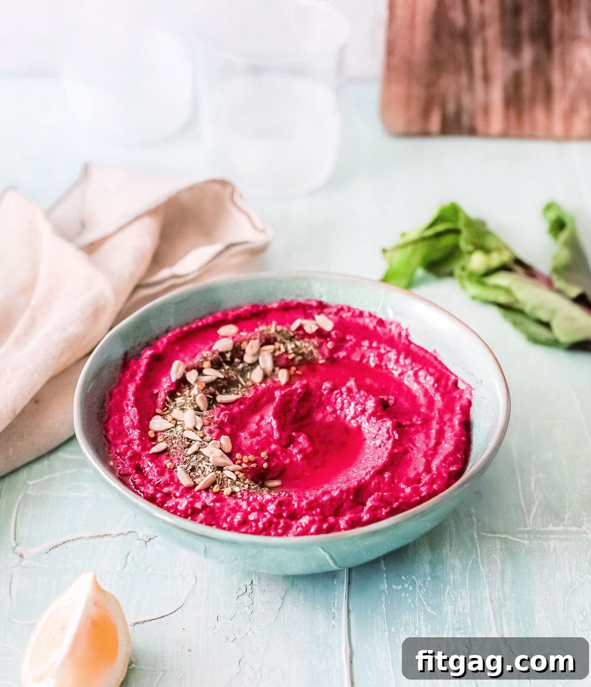 Vibrant Beet Hummus: Your Everyday Delight 4 A bowl of roasted beet hummus, generously garnished with a variety of seeds and a swirl of olive oil, set against a backdrop of a soft beige towel and a rustic wooden board, creating an inviting and warm culinary scene.