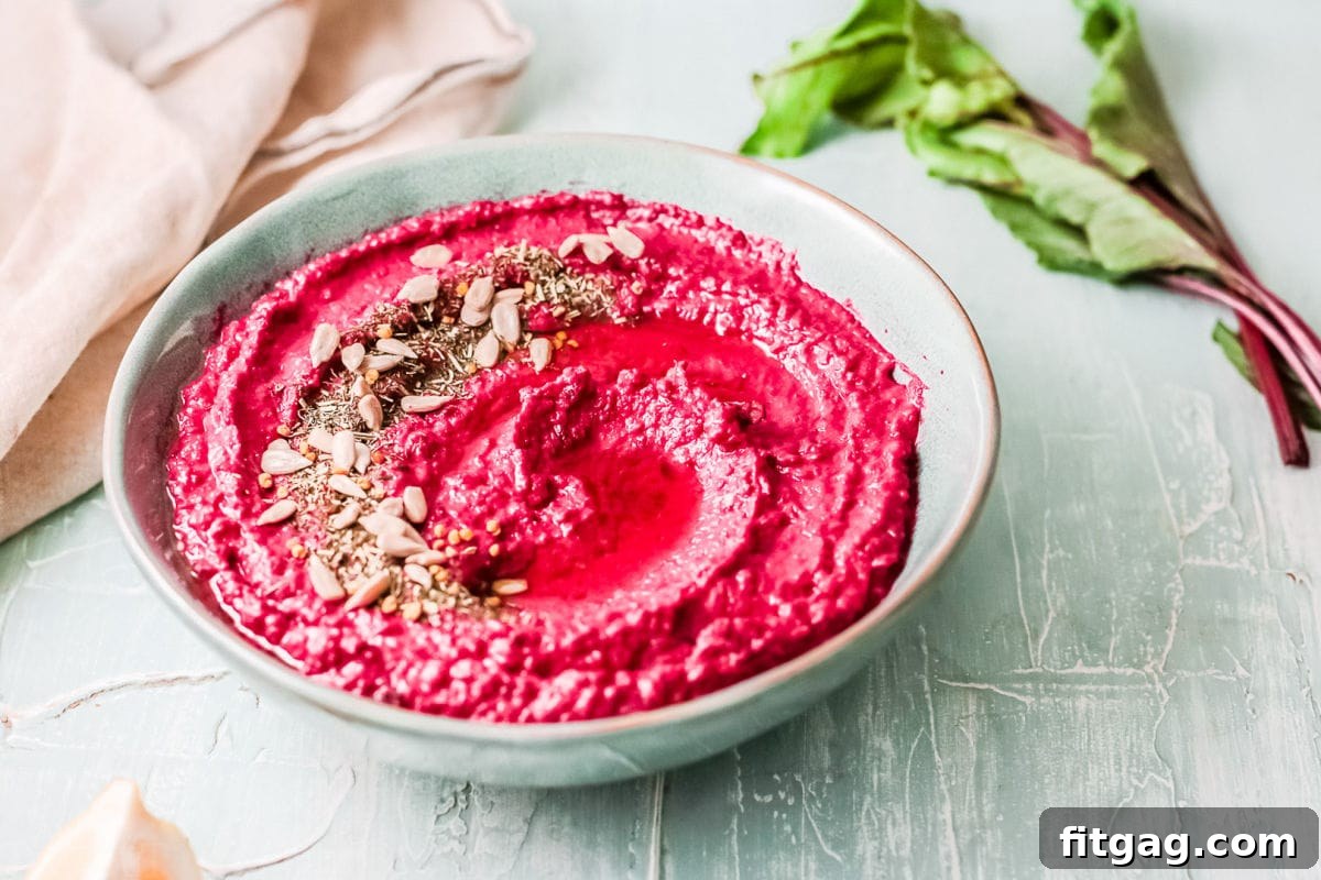 Vibrant Beet Hummus: Your Everyday Delight 5 Easy beet hummus presented in a large blue-green bowl, artfully garnished with a swirl of olive oil and a sprinkle of various seeds, demonstrating its rich, creamy texture and vibrant color.