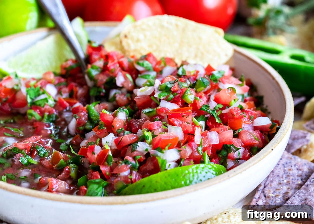 close up look at pico de gallo all mixed up in a medium sized clay bowl with chips around it.  
