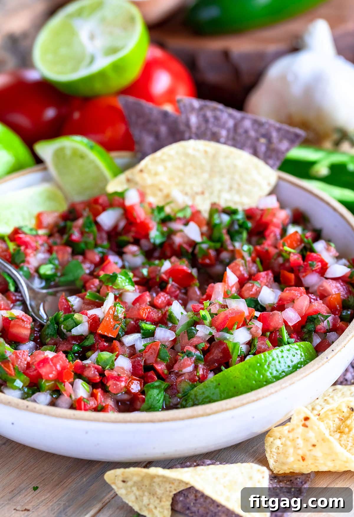 bowl of salsa fresca with some removed. spoon and a few chips are in the bowl.