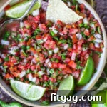 top down view of pico de gallo in clay bowl garnished with lime wedges and surrounded by chips.