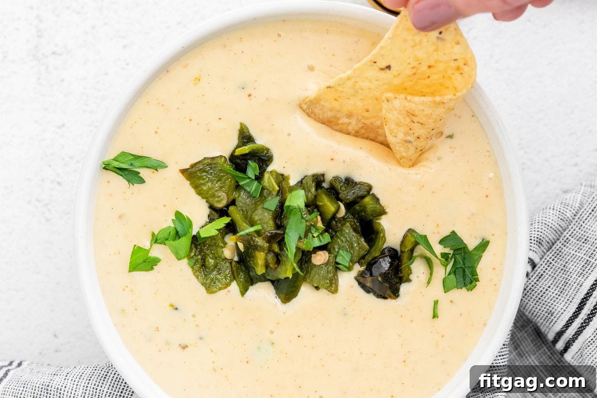 Irresistible Queso Blanco Dip 3 top down look at queso blanco in a white bowl topped with cilantro and peppers with a chip being dipped into the queso.