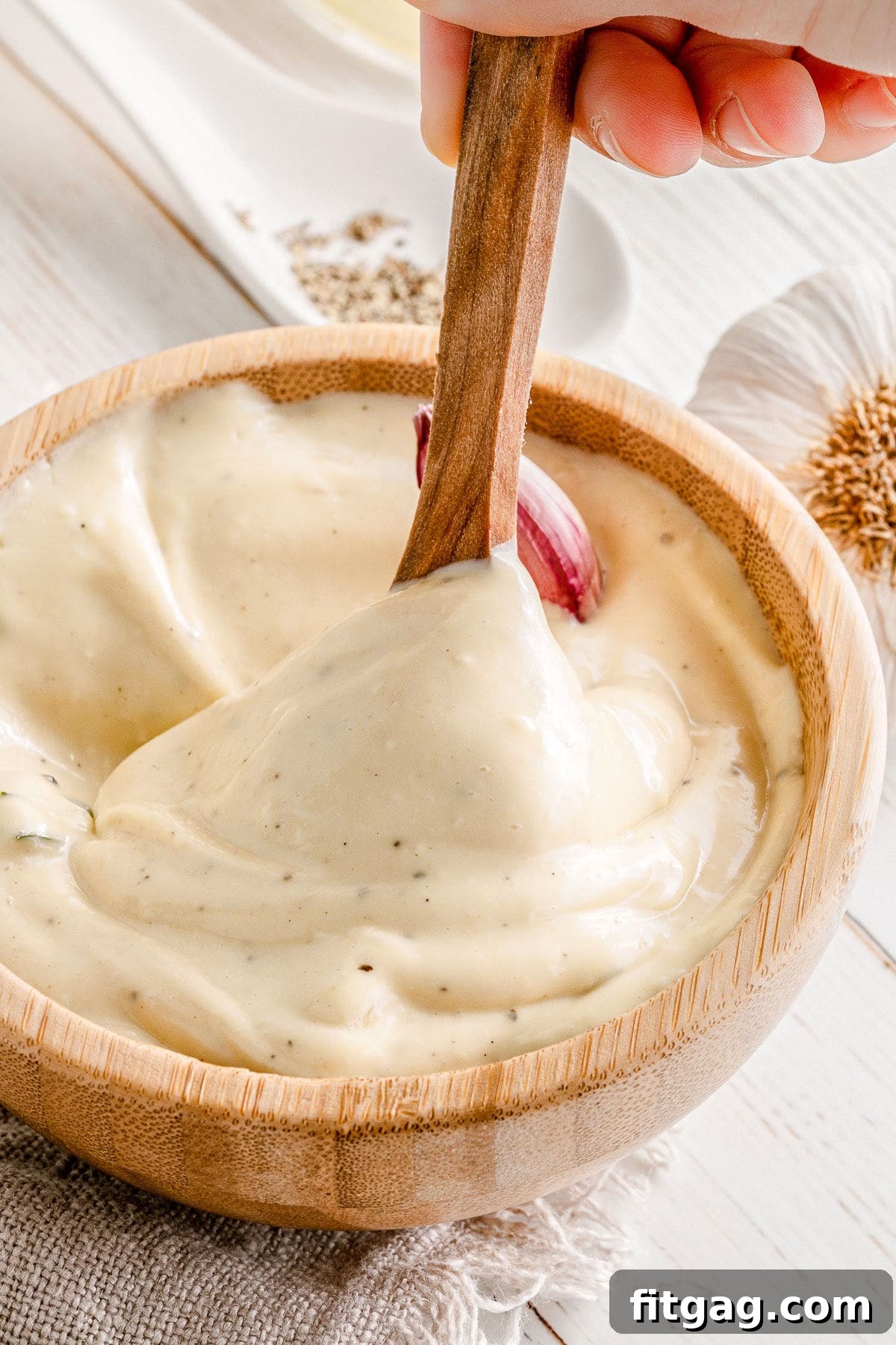 A wooden spoon dipped into creamy garlic aioli in a small wooden bowl, highlighting its smooth texture.