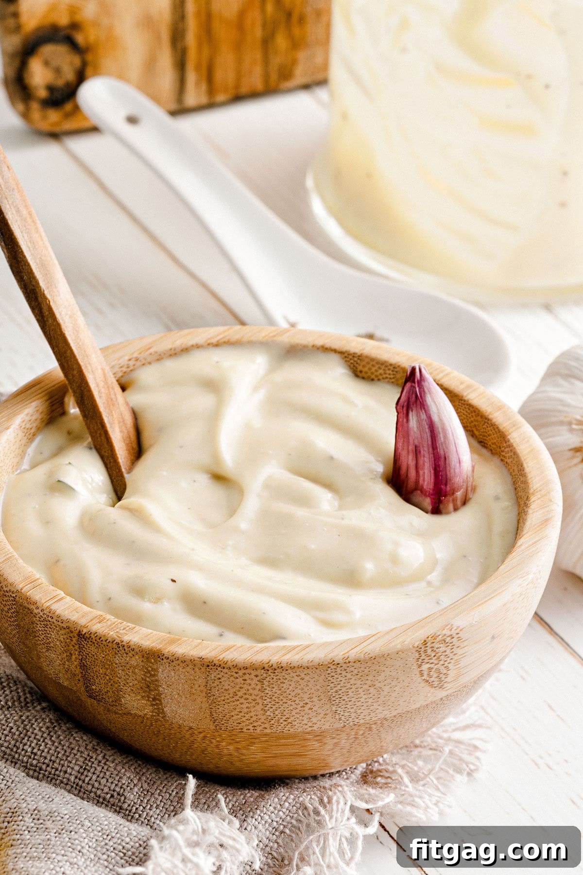 Garlic aioli served in a wooden bowl with a spoon and a garlic clove resting on top, ready to be enjoyed.